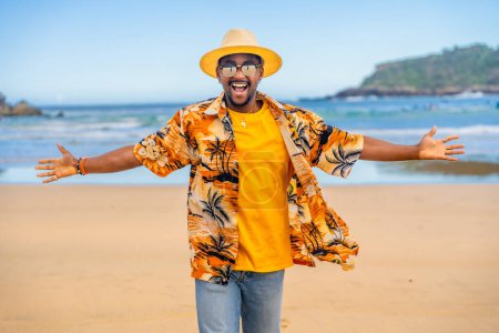 Afro cool man in colorful clothes embracing holidays opening arms walking at beach