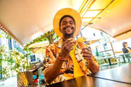 Low angle view portrait of a smiling african american tourist sitting on a terrace eating ice cream