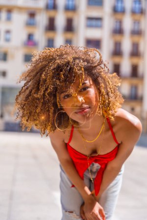Vertical portrait of a latin young woman with curly hair bending sensual to look at camera in the city