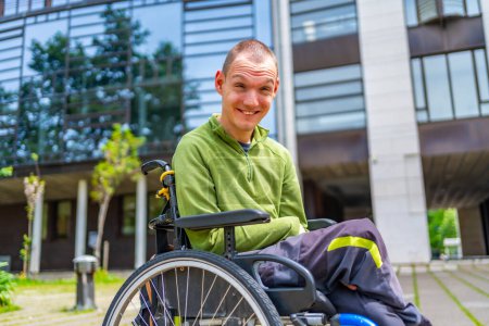 Glücklicher behinderter erwachsener Mann im Rollstuhl lächelt vor der Universität in die Kamera