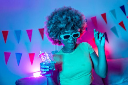 Cool african woman with sunglasses dancing, drinking cocktail and partying at home