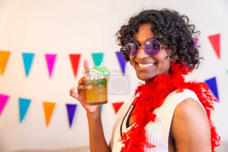 Cool young latin man holding cocktail glass and smiling at camera partying at home