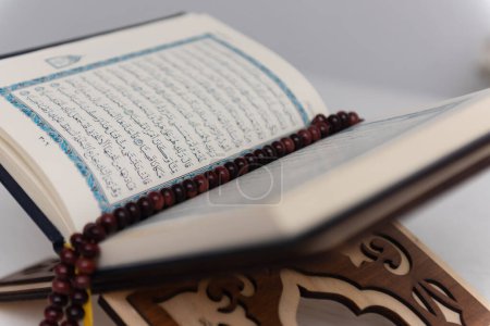 Foto de The words on Qoran is arabic words which means the Holy Qoran. Muslim beads and Koran on wooden table. Islamic concept. - Imagen libre de derechos