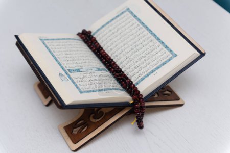 Foto de The words on Qoran is arabic words which means the Holy Qoran. Muslim beads and Koran on wooden table. Islamic concept. - Imagen libre de derechos