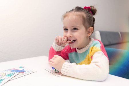 Téléchargez les photos : Jolie fille européenne ou américaine de 4 ans jouant à côté de puzzles tout en étant à la maison en hiver. Joyeux Sur la table il y a des jouets - en image libre de droit