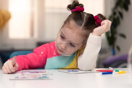 Foto de Prety 4 años de edad niña europea o americana jugando al lado de rompecabezas mientras está en casa en el invierno. Alegre En la mesa hay juguetes - Imagen libre de derechos
