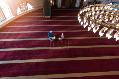 Téléchargez les photos : L'homme musulman enseigne à son petit fils à prier Allah et lui enseigne à lire le Coran à la mosquée pendant le ramadan. - en image libre de droit
