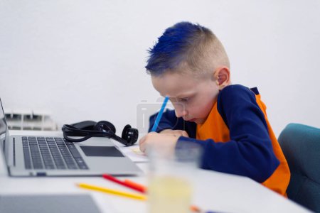 Téléchargez les photos : Adorable enfant faisant ses devoirs et utilisant un ordinateur portable et des gadgets modernes. Concept d'enseignement à domicile. - en image libre de droit