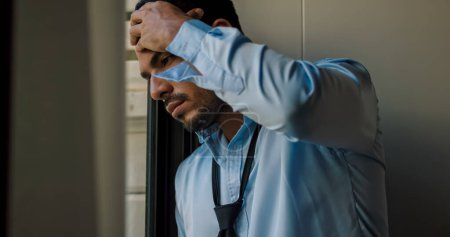 A businessman is standing by the window depressed and stressed with problems in his life.