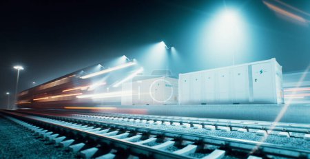 A long-exposure nighttime image showing an electrical energy storage system through a battery energy storage unit in an industrial railway environment, showing a speeding train in motion. 3d rendering.