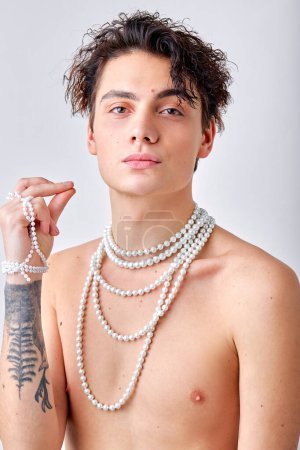 Photo for Portrait of shirtless naked guy with tattoo and natural make-up, with chain necklace posing at camera as professional model. Caucasian guy isolated over white studio background. models, beauty - Royalty Free Image