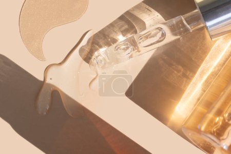 close up of pipette with pouring liquid serum with golden bottle and shadows on beige background