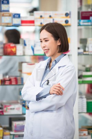 Téléchargez les photos : Vue latérale du sourire pharmacien asiatique femme debout au comptoir à la pharmacie, Service médical de professionnel. - en image libre de droit