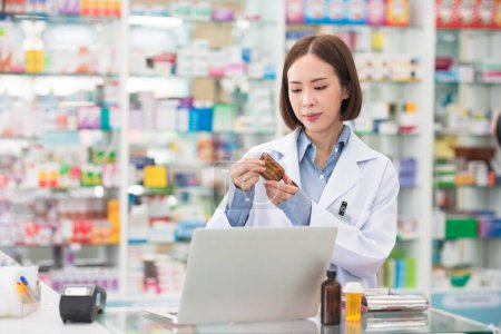 Photo for Professional pharmacist asian woman smiling at counter using laptop computer for check medicine inventory in drug store, Medical service online, Telemedicine to giving medical information to patient. - Royalty Free Image