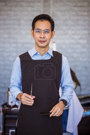 Téléchargez les photos : Portrait de coiffeur asiatique souriant debout dans le salon de coiffure et salon de coiffure - en image libre de droit