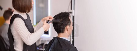 Photo for Asian woman hairstylist using scissors and comb for hair cut and design on man's hair in barbershop. - Royalty Free Image