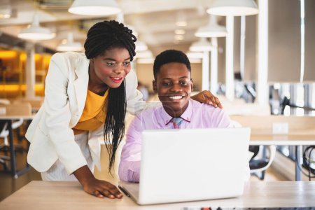 Téléchargez les photos : Sourire jeune homme d'affaires afro-américain et femme d'affaires utilisant un ordinateur portable tout en discutant du nouveau plan de projet. - en image libre de droit