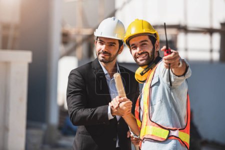 Photo for Teamwork men in construction site, Two civil engineer in safety helmet hard hat using digital tablet and blueprint working while standing at factory. - Royalty Free Image