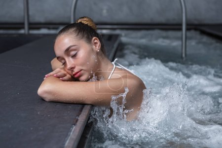 Photo for Relaxed young woman closing eyes and holding head on crossed arms while chilling in splashing water of massage pool on weekend day on spa resort - Royalty Free Image