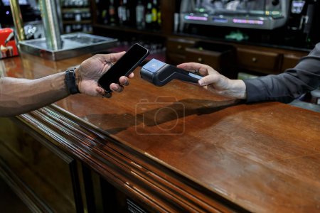 Ein Mann in einer Bar bezahlt mit seinem Smartphone auf dem Datentelefon des Barkeepers.