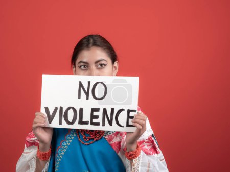 chica latina en traje de kichwa sosteniendo un cartel con un mensaje de "no violencia" sobre un fondo rojo