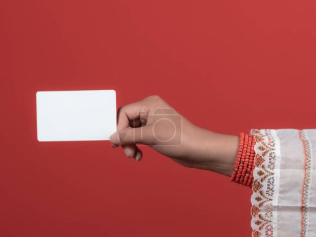 Téléchargez les photos : Main de femme kichwa avec poignées rouges tenant une carte de crédit avec fond rouge - en image libre de droit