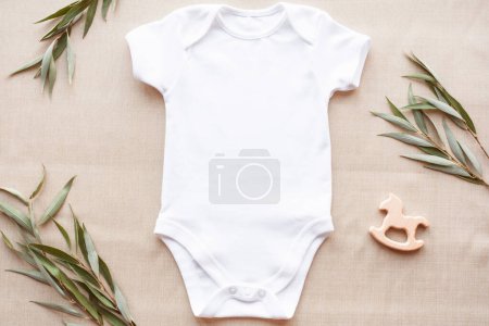 Téléchargez les photos : Maquette de body bébé blanc sur lin avec verdure et jouet. Modèle de vêtements de bébé vierges dans le style de la ferme, plat. - en image libre de droit