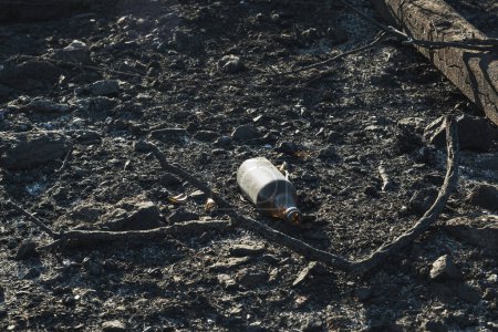 Foto de Primer plano de una botella de cerveza después de un incendio forestal en las cenizas. - Imagen libre de derechos