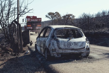 Photo for Izmir, Turkey - July 23, 2022: Rear view of Burnt car with a firetruck in front of it aftermath the forest fire at Derya Site Seferihisar Izmir Turkey. - Royalty Free Image