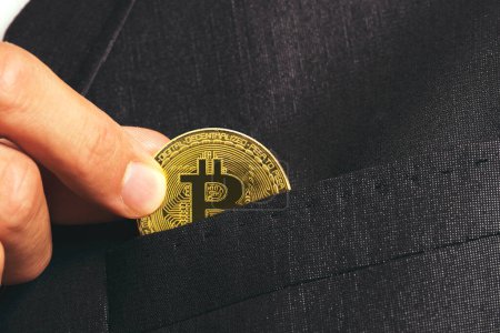 Izmir, Turkey - August 11, 2022: Businessman's Hand holding a bitcoin to put in suit's pocket.