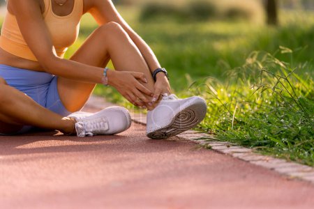 Foto de Primer plano de una mujer de 20 años en una pista de atletismo con tops amarillos y medias azules sosteniendo su tobillo con dolor. - Imagen libre de derechos