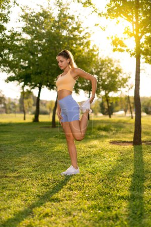 Photo for A woman with a yellow top and blue tights stretching and warming up in a public park in the morning. - Royalty Free Image