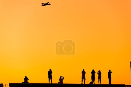 Photo for Silhouette of some photographer people taking photo of an acrobatic plane on sunset. - Royalty Free Image