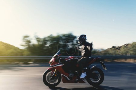 Side view of a motorcycle rider riding red race motorcycle on the highway with no hands and with motion blur. 