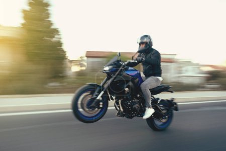Foto de Vista lateral de un motociclista que monta la motocicleta de la raza en un wheelie la carretera con el desenfoque del movimiento. - Imagen libre de derechos