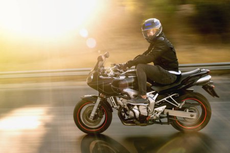 Foto de Vista lateral de un motociclista que monta la motocicleta roja de la raza en la carretera con desenfoque del movimiento. - Imagen libre de derechos