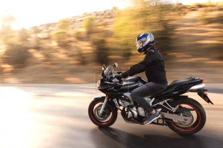 Téléchargez les photos : Vue latérale d'un motard chevauchant une moto de course noire sur l'autoroute avec flou de mouvement. - en image libre de droit