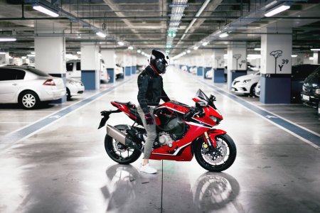 Photo for Side view of race motorcycle rider with a helmet in a car parking lot. - Royalty Free Image