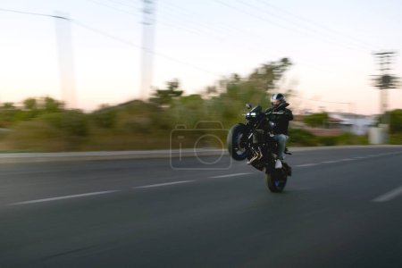 Photo for Motorbike rider doing wheelie on the road in the evening. - Royalty Free Image