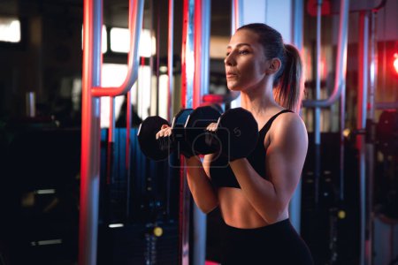 Photo for Portrait of a woman doing shoulder press with dumbells in a gym. - Royalty Free Image