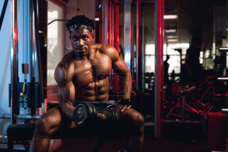 Foto de 20s Black and muscular man in a gym doing concentration curls with dumbbell - Imagen libre de derechos
