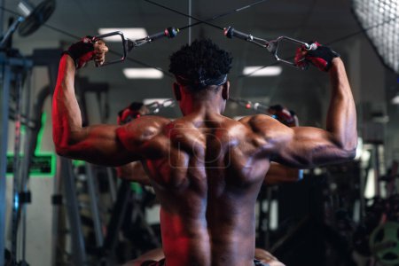 Foto de 20s Masculino negro ejercitando los músculos posteriores delt y espalda con máquina de cable - Imagen libre de derechos