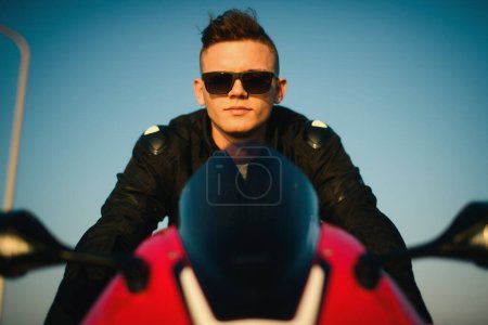 Téléchargez les photos : Portrait d'un jeune homme avec des lunettes de soleil sur une moto de course rouge. - en image libre de droit