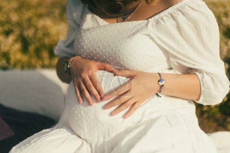 Foto de En un primer plano de su vientre, una mujer embarazada forma un corazón con sus manos, una encantadora mariquita descansando sobre su piel, un símbolo de amor y buena suerte - Imagen libre de derechos
