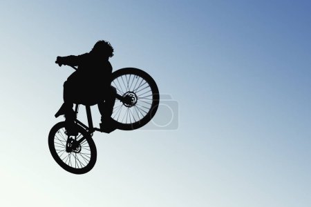 Foto de Un ciclista a mitad de salto, en silueta contra el cielo abierto. La imagen captura la emoción del ciclismo - Imagen libre de derechos