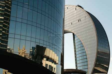 Foto de Bakú, Azerbaiyán - 26 de junio de 2023: Foto de madrugada del Hotel Crescent y un rascacielos vecino en Bakú el 26 de junio de 2023. La superficie reflectante del rascacielos de cristal moderno captura impresionantes reflejos como espejos de las ciudades circundantes - Imagen libre de derechos