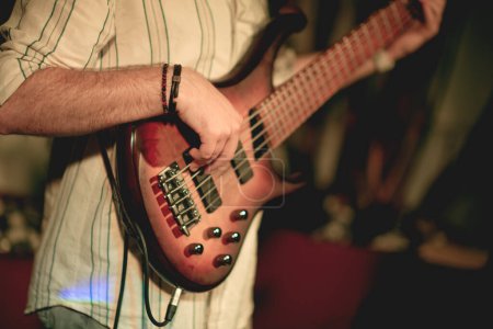 Photo for A close-up shot of a bass guitar being played by a young man in his twenties. The focus is on the instrument, with the player's face not visible, emphasizing the hands and the strings. - Royalty Free Image