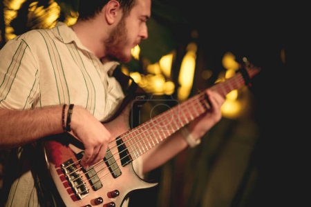 Photo for A close-up shot capturing a young male bassist in his twenties as he plays his instrument. His expression is visible, revealing the passion and intensity he brings to his performance - Royalty Free Image