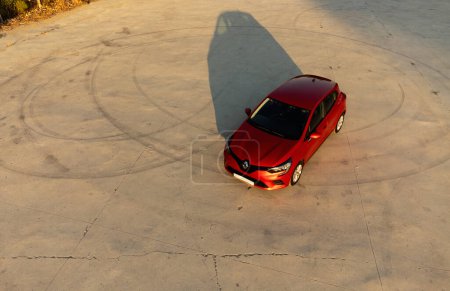 Téléchargez les photos : Izmir, Turquie - 2 août 2023 : Vue par drone d'une Renault Clio 5 rouge sur béton avec marques de dérive. Les tons chauds du coucher du soleil mettent en évidence l'ombre de la voiture - en image libre de droit