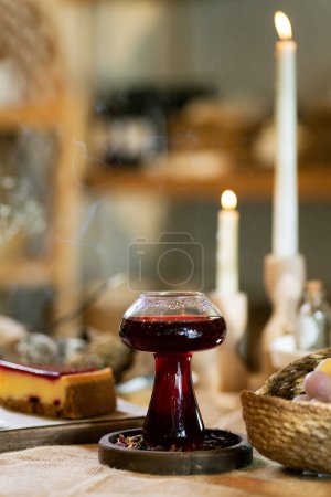Photo for A warm scene showcasing a slice of strawberry cheesecake on a wooden board next to a cup of winter tea. Set on a burlap tablecloth under ambient candlelight, this setting embodies comfort and indulgence. - Royalty Free Image
